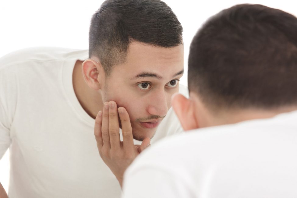young man looking in mirror for acne