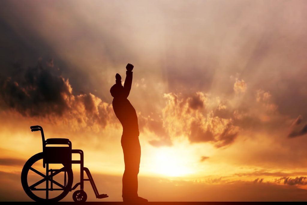 man standing up from wheelchair against the sunset