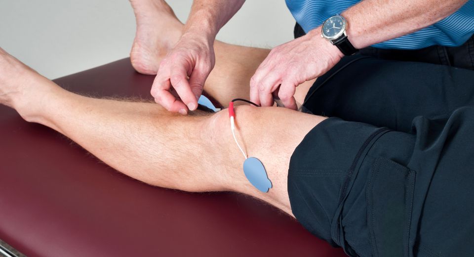 A physical therapist putting on muscle stimulator on a patient's knee.