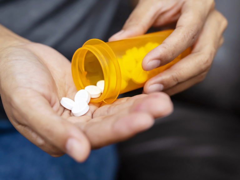 Photo of a pill bottle with pills going out from the bottle into someone's hand